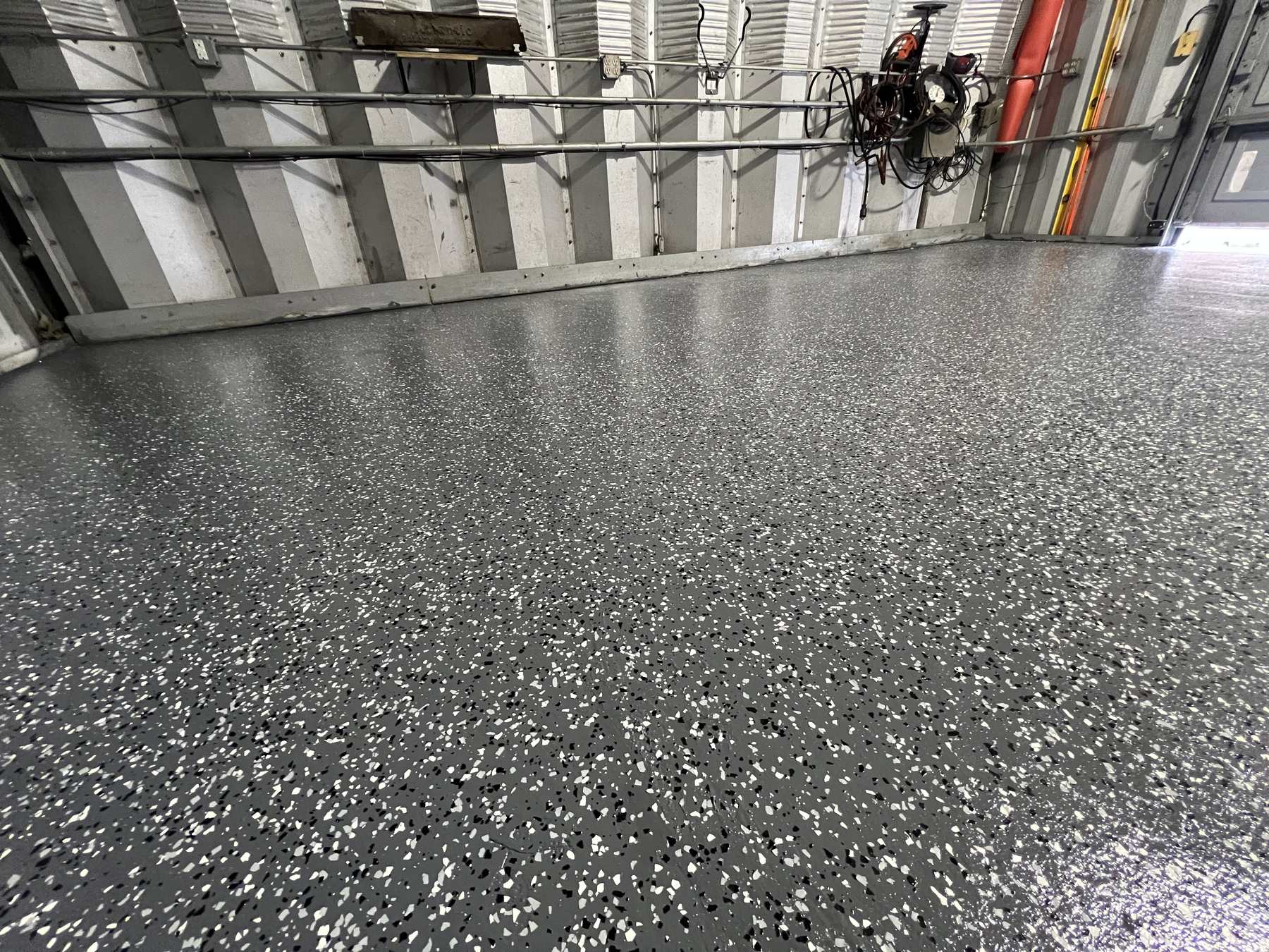 Grey flake epoxy floor with a glossy finish along the corrugated metal wall of a garage or shop