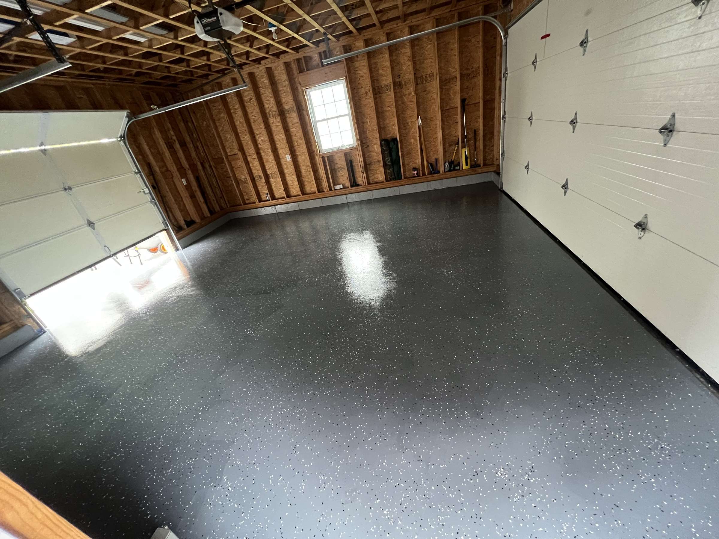 Glossy grey flake epoxy floor in a finished garage with wood-framed walls, two overhead doors and a window