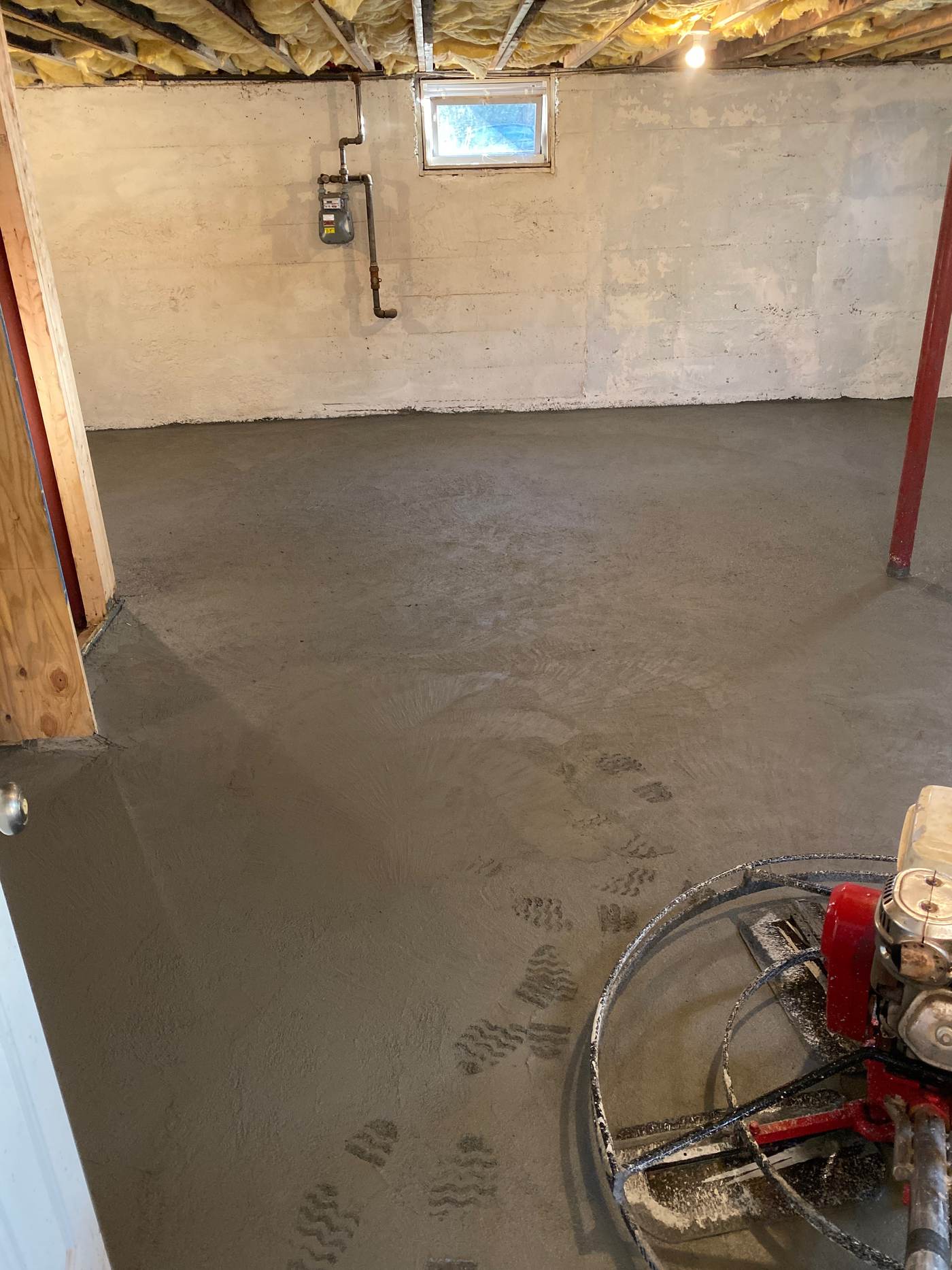 New concrete basement floor with a power trowel machine in the corner and footprints in the fresh surface