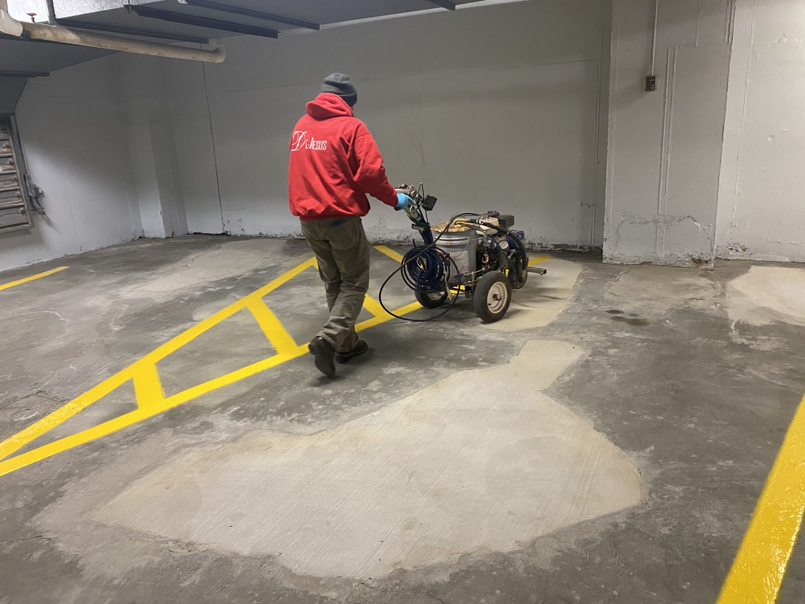 Worker pushing a line striping machine to paint yellow lines on the concrete floor of an indoor parking garage